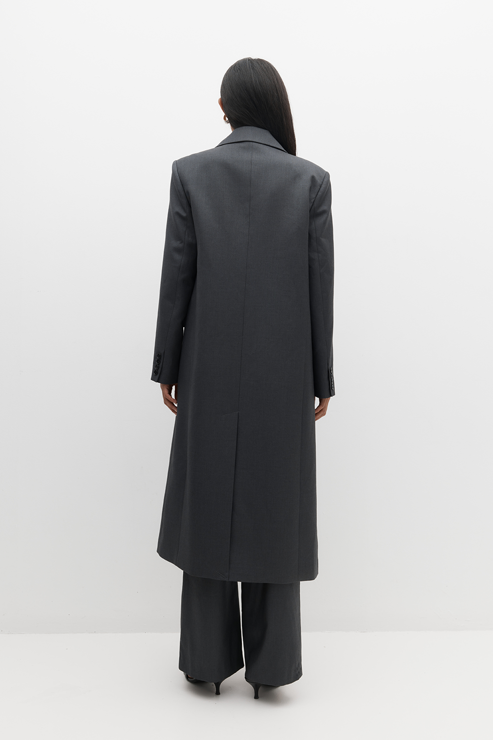 Rear angle of the REBE Icon Coat styled on a model, highlighting longline cut and minimal seam detailing.